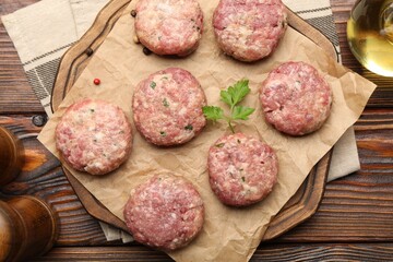 Raw meat patties with parsley and peppercorns on wooden table, flat lay