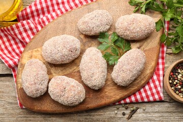 Uncooked meat patties, parsley and peppercorns on wooden table, flat lay