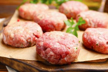 Raw meat patties on wooden board, closeup