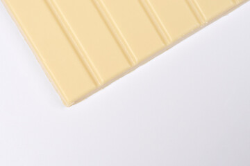 A close-up shot shows a corner and portion of a white chocolate bar with vertical grooves on a minimalist grey-white background with copy space