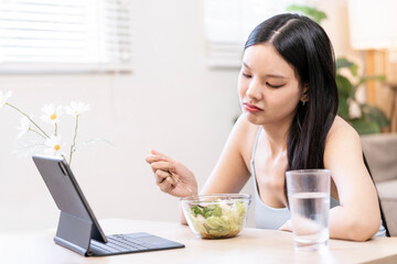 Young woman focusing on a video or work on a tablet while having a healthy salad lunch at home.