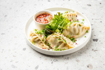 Steamed dumplings with herbs and chili sauce on a white plate, garnished with lettuce and microgreens. Asian appetizer, clean presentation, top view.