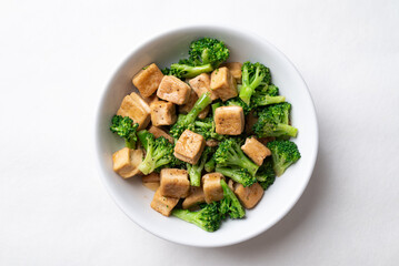 Stir fried tofu and broccoli with soy sauce in bowl on white background, Asian vegan food, Top view