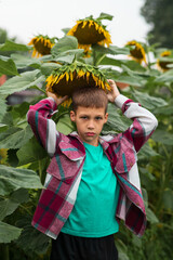 a portrait of a boy with dark hair and a sad face, holding a bright yellow sunflower on his head