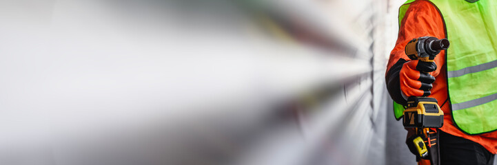 Close-up of a construction worker in a reflective vest and protective gloves holding a cordless...