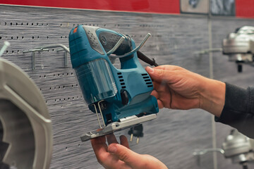 Close-up of hands holding an electric jigsaw in a hardware store, selecting a power tool for woodworking or repair. Concept of construction equipment and DIY projects.