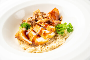 A gourmet dish of sliced roasted chicken breast with mushrooms and fresh parsley, served on a bed of creamy orzo pasta in a white bowl.