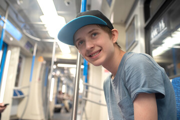 A teenage boy in a T-shirt and cap sits in a train carriage