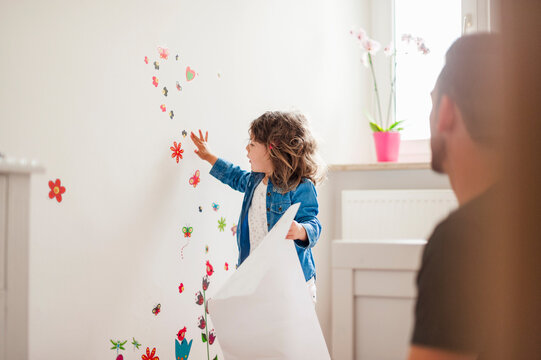 Father and daughter decorating wall with stickers at home