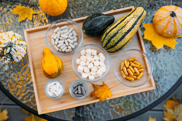 Outdoor flatlay of fall gourds and various supplements in glass bowls arranged on a wooden tray over autumn leaves. Functional nutrition in natural contexts, whole food supplements, seasonal wellness