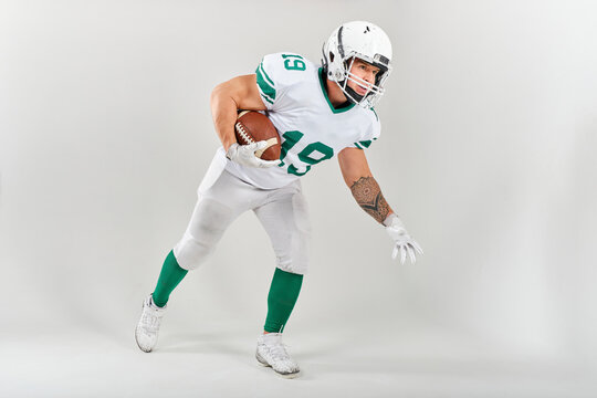 Full-length portrait of American football player in uniform holding ball