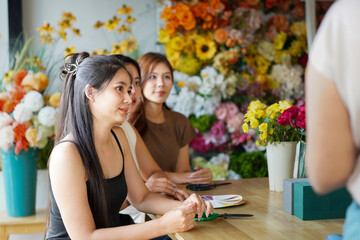 Diverse group of young people arranging flowers in florists workshop while attending class on floral art