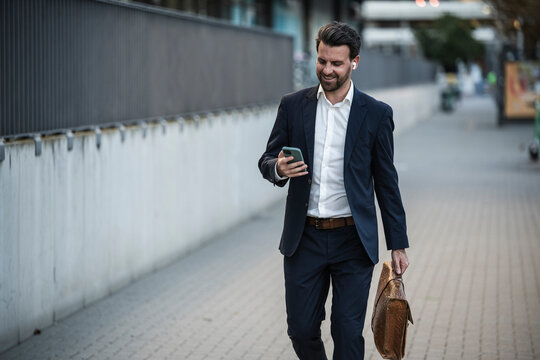 Businessman with briefcase using mobile phone walking on footpath