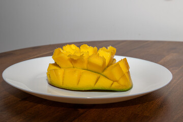 Juicy yellow mango cubes with whole mangoes on a white plate. Vegetarian.