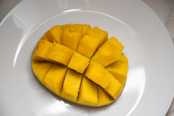 Juicy yellow mango cubes with whole mangoes on a white plate. Vegetarian.
