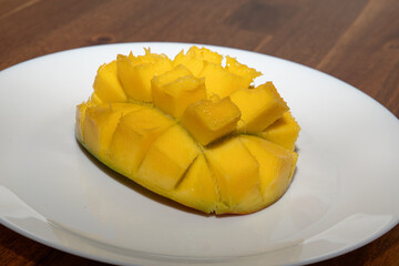 Juicy yellow mango cubes with whole mangoes on a white plate. Vegetarian.