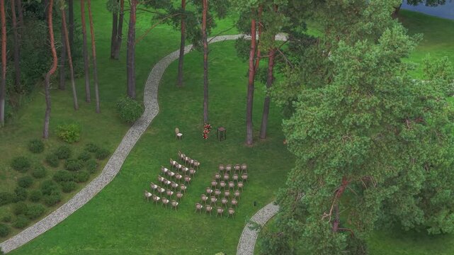 Aerial shot of an intimate wedding ceremony setup in a serene forest with chairs arranged in rows among tall trees and winding stone paths.