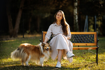Naklejka premium Woman sitting on bench with fluffy sheltie dog in garden