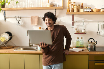 Handsome young man enjoying his time in the kitchen while working on a laptop