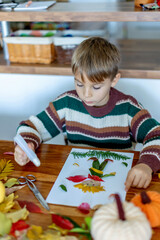 Sweet child, boy, applying leaves using glue while doing arts and crafts at home