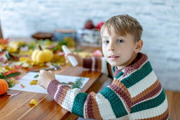 Sweet child, boy, applying leaves using glue while doing arts and crafts at home