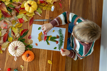 Sweet child, boy, applying leaves using glue while doing arts and crafts at home
