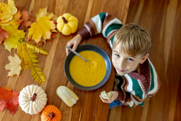 Sweet child, boy, eating pumpkin soup, applying leaves using glue while doing arts and chraft with leaves