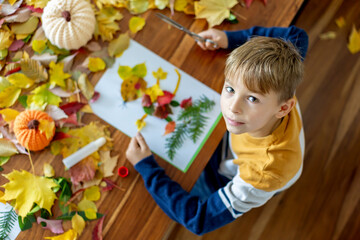 Sweet child, boy, applying leaves using glue while doing arts and crafts at home