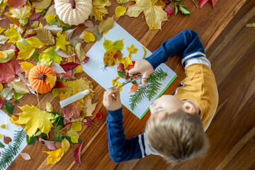Sweet child, boy, applying leaves using glue while doing arts and crafts at home
