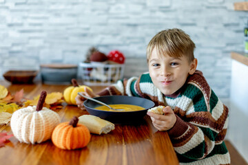 Sweet child, boy, eating pumpkin soup, applying leaves using glue while doing arts and chraft with leaves