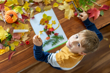 Sweet child, boy, applying leaves using glue while doing arts and crafts at home