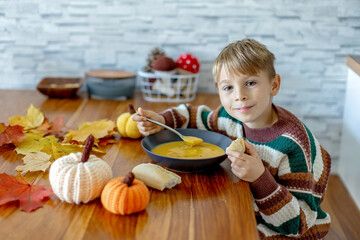 Sweet child, boy, eating pumpkin soup, applying leaves using glue while doing arts and chraft with leaves