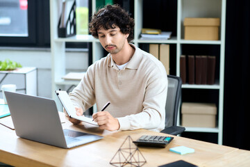 Fototapeta premium Handsome young man focused on his work while sitting at a modern desk in a stylish office