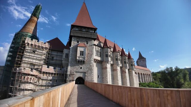 Corvin Castle, a significant Gothic-Renaissance landmark in Transylvania, Romania, stands under a clear blue sky, presenting its architectural grandeur and ongoing restoration work on prominent tower