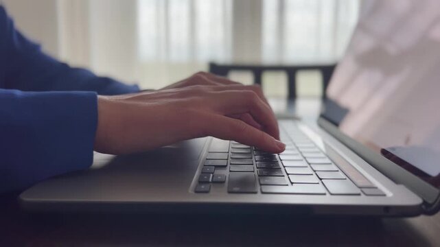 Close-up shot of human hands typing on a sleek laptop in a bright home workspace. Symbol of digital lifestyle, communication, productivity, freelance job and online business. Ideal for concepts of rem