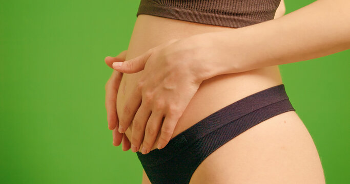 Side view of pregnant women caressing her belly over green screen background. Young expecting mother holding baby in pregnant stomach.