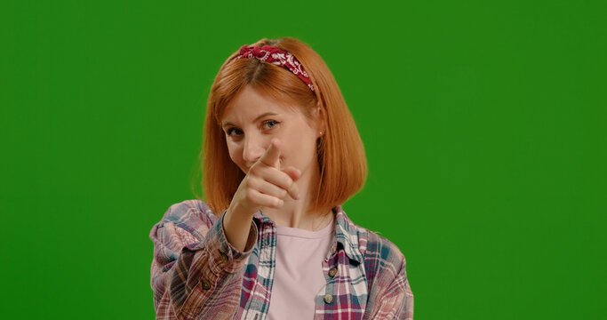 I am watching you gesture shown by woman pointing at her eyes and camera on green screen background. Casual dressed female spying on someone.