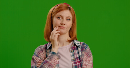 Annoyed woman in plaid shirt listens with skeptical expression on green screen background. Bored...