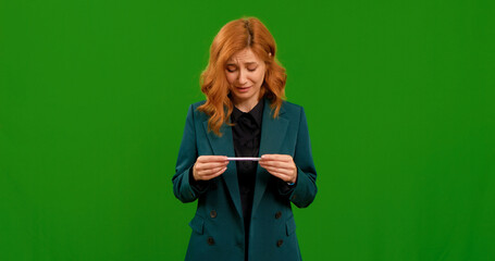 A woman stands in front of a green backdrop, showing different gestures as she examines a test. Her expressions range from joy to concern, conveying a strong emotional response.