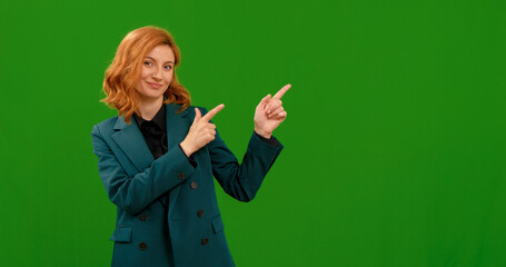 Woman looking into the camera, smiling showing to the left gestures with hands on green chroma key screen background. Female hand sign left, direction showing in front of chroma key.