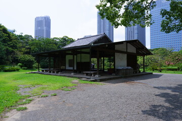 Obraz premium A traditional wooden teahouse or rest shelter in a Japanese public garden, with modern high-rise buildings in the background