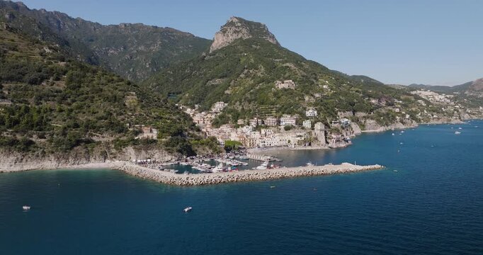 Aerial view of the Erchie harbor with its stone pier jutting into the turquoise sea against a backdrop of lush green mountains, Erchie, Amalfi Coast, Italy.
