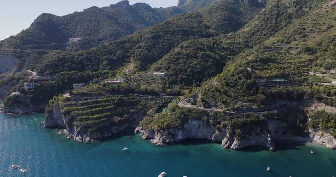 Aerial view of the rugged coastline meeting the lush green mountains, a small boat floats on the turquoise water, Erchie, Amalfi Coast, Italy.