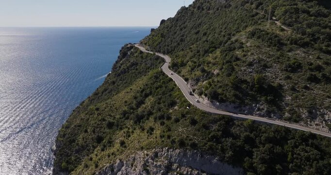 Aerial view of a winding road along the lush, green Erchie coastline contrasting with the deep blue sea on a sunny day, Erchie, Amalfi Coast, Italy.
