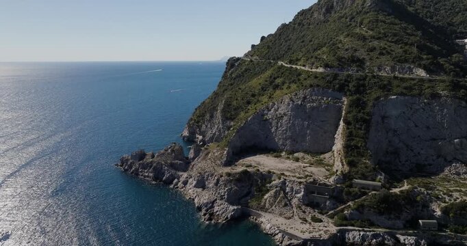 Aerial view of the rugged Erchie coastline with steep cliffs meeting the turquoise sea, showcasing a winding road and lush vegetation, Erchie, Amalfi Coast, Italy.