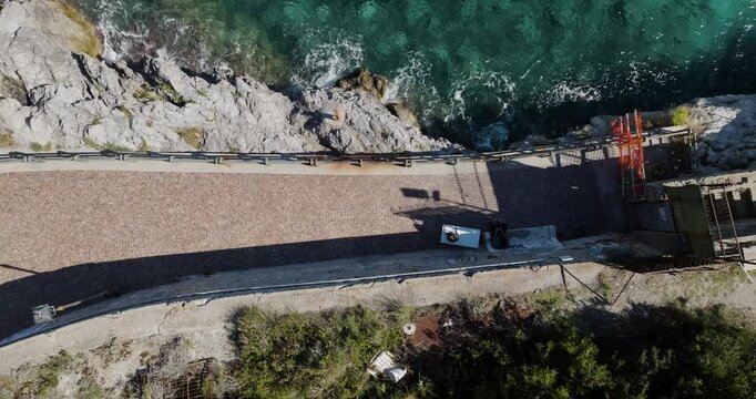 Aerial view of a winding coastal road next to the turquoise sea, contrasting with the rugged rocks and greenery, Erchie, Amalfi Coast, Italy.
