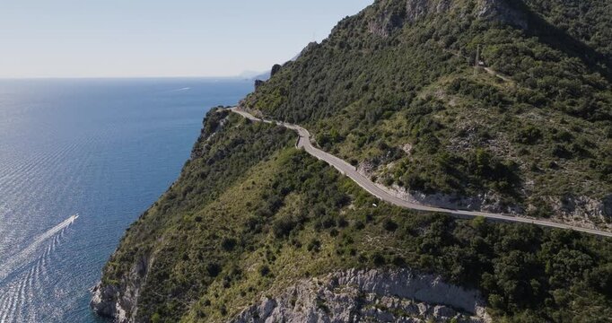 Aerial view of a winding coastal road clinging to a steep mountainside, where the green foliage contrasts with the deep blue sea, Erchie, Amalfi Coast, Italy.