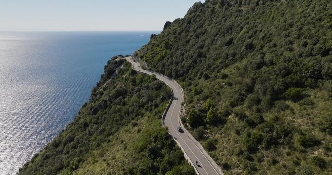 Aerial view of the vivid contrast between the deep blue sea and the lush green hillside road with cars, Erchie, Amalfi Coast, Italy.
