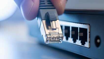 A person plugging an ethernet cable into a network switch port. Macro shot of an RJ45 connector establishing an internet connection. LAN networking and data communication concept