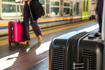 Traveler with black suitcase waiting at train station platform, surrounded by other passengers